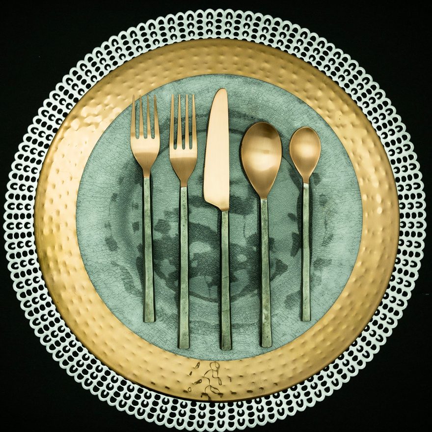 Brushed-brass flatware on a sage ceramic plate with a beaded charger