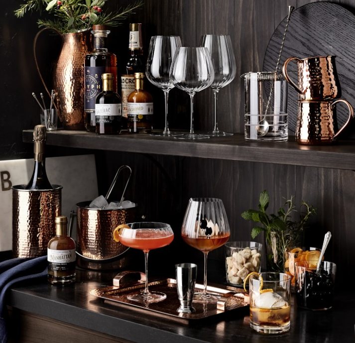 Hammered copper barware styled on a dark bar cart